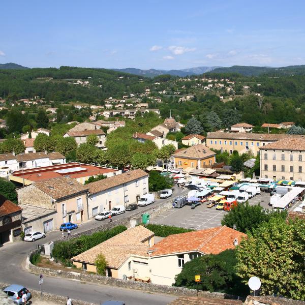 Vue en hauteur du marché de Joyeuse en Ardèche, avec ses étals installés sur la place du village.
