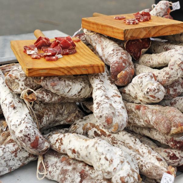Étal de charcuterie sur un marché en Ardèche, avec saucissons artisanaux et morceaux à déguster.
