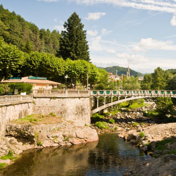 Vue de Vals-les-Bains en Ardèche, avec son pont au-dessus de la rivière et les bâtiments du centre-ville en arrière-plan.
