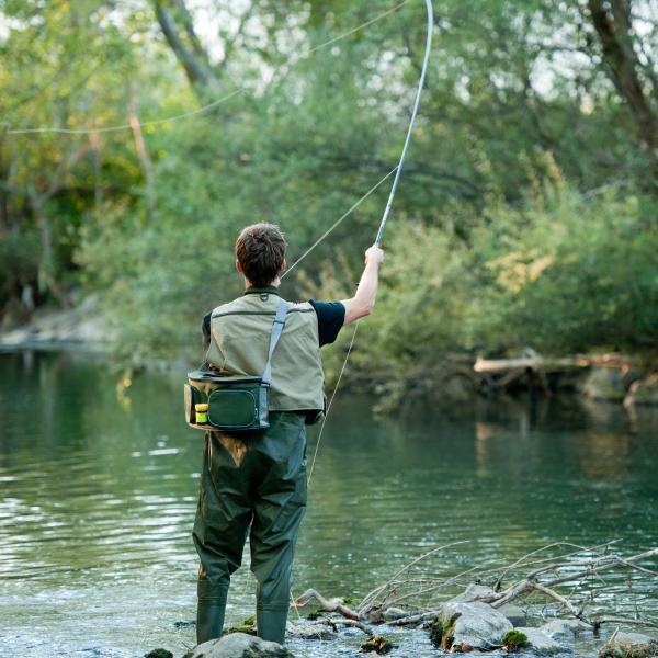 Pêcheur à la mouche dans la rivière Ardèche, debout sur des rochers, entouré de végétation luxuriante.
