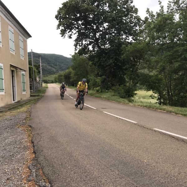 Cyclistes roulant sur une route en Ardèche, dans un paysage vallonné et verdoyant.
