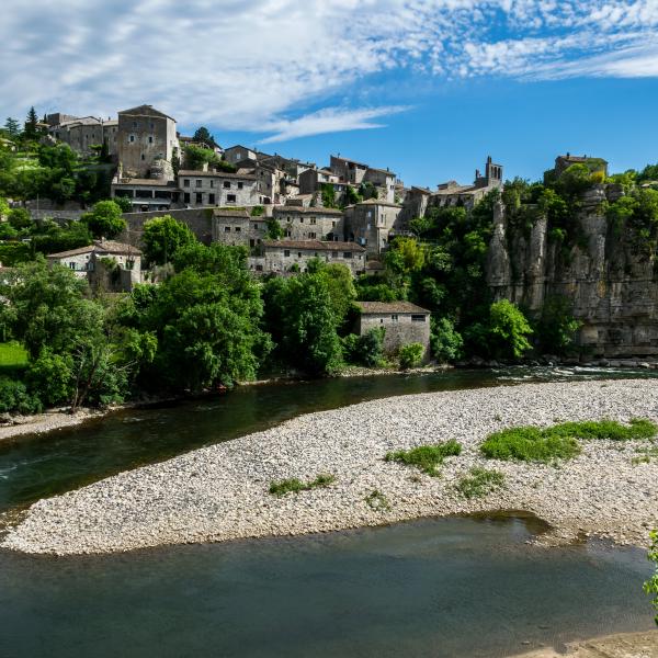 Vue de Balazuc, beau village français avec maisons en pierre, falaise, rivière et verdure.
