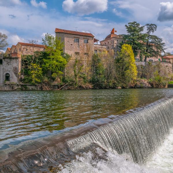 Vue pittoresque de Ruoms en Ardèche, avec ses bâtiments en pierre et une cascade sur la rivière.